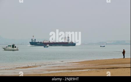 Ein Mann, der vom Strand aus angeln kann, als Cemvale Cement Carrier Frachtschiff, das den Hafen von Santander an einem ruhigen, nebligen Wintermorgen Santander Cantabria Spanien verlässt Stockfoto