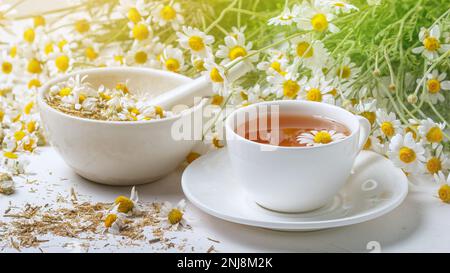 Ländliche Stillleben - Tasse gebrühten Kamillentee auf dem Hintergrund eines Straußes von Gänseblümchen, Nahaufnahme Stockfoto