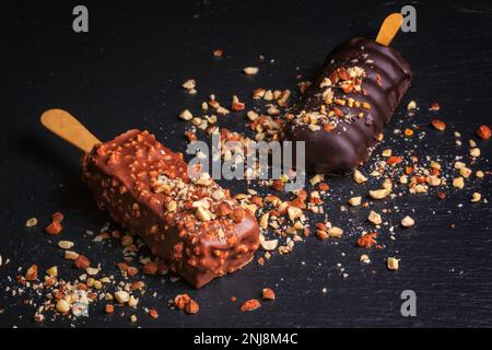 Schokoladenkuchen knallt mit Nüssen in Form von Popsicle auf Stick auf schwarzem Schiefertafel Hintergrund Stockfoto