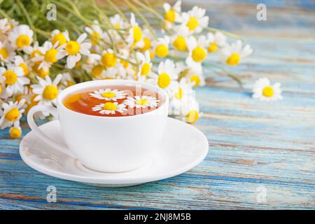 Gänseblümchen blüht in einer weißen Tasse Tee, Kamillenkräuter auf Holzgrund. Kräutermedizin. Gesundes Lifestyle-Konzept. Stockfoto