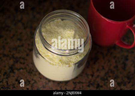 Glasbehälter mit Milchpulver und rotem Becher. Tageslicht. Stockfoto