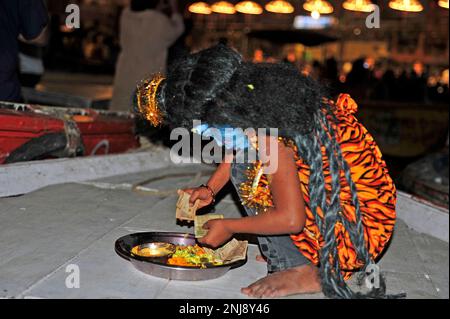 Kleines Mädchen in traditionellem Kostüm und Gesicht, gemalt als Hindu-gott Shiva, sammelt Geld von Touristen. Varanasi - Indien Stockfoto