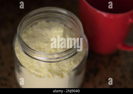 Glasbehälter mit Milchpulver und rotem Becher. Tageslicht. Stockfoto
