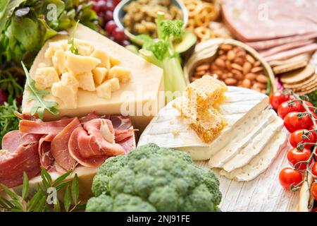 Brie und Parmesankäse mit Honig aus der Nahaufnahme. Tisch voller mediterraner Vorspeisen, Tapas oder Antipasto. Auswahl an italienischen Speisen. Köstlicher Snack Stockfoto