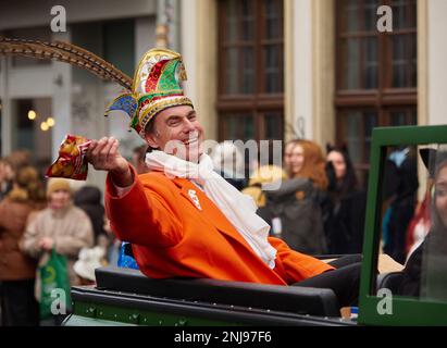 Würzburg, Bayern, 19. Februar 2023. Mann mit Karnevalsmütze mit Feder und orangefarbenem Mantel, der den Zuschauern bei der Karnevalsparade (Fasching) ein Päckchen Süßigkeiten wirft Stockfoto