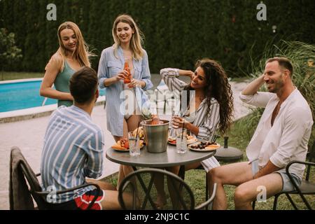 Eine Gruppe junger Erwachsener, die eine gemütliche Sommerparty mit Essen und Getränken im Hinterhof genießen Stockfoto