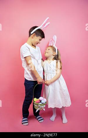 Ein Mädchen und ein Junge mit Hasenohren sehen sich an und halten einen Korb Eier Stockfoto