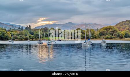 Yachten liegen am Lake Windemere bei Sonnenuntergang vor, mit Berggipfeln im Hintergrund Stockfoto