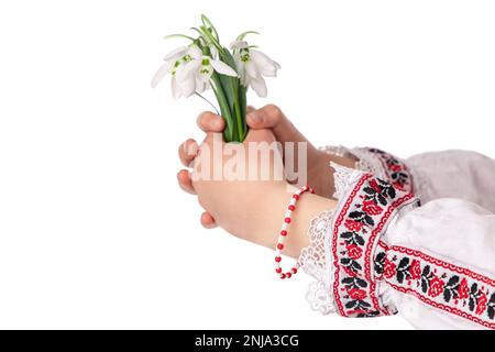 Bulgarisches Mädchen in traditionellen Folklore-Kostümen mit Frühlingsblumen, Schneetropfen und handgefertigtem Wollarmband Martenitsa Symbol von Baba Marta Stockfoto