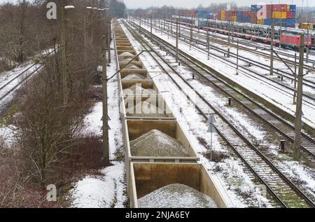 Eisenbahnwaggons mit Kies, die auf Abstellgleisen geparkt sind. Im Hintergrund sind Container und Wagen, die mit Autos beladen sind, unscharf. Stockfoto