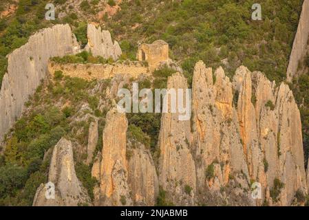 Details der Roques de la Vila in Finestres (auch bekannt als Muralla de Finestres) und der Einsiedlung von San Vicente zwischen den Felsen bei Sonnenuntergang, Spanien Stockfoto