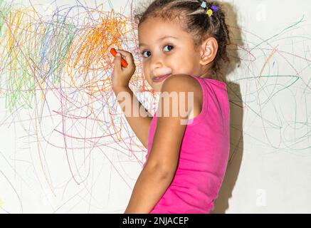 Kleines brasilianisches Mädchen kritzelt, malt und malt auf hellgelber Wand Stockfoto