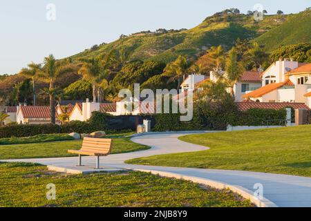 Fußweg entlang der Küste und hölzerne Bank mit Blick auf den Ozean, und wunderschöne Häuser und grüne Hügel im Hintergrund, Kalifornien Stockfoto