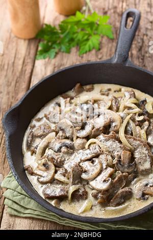 Frisches hausgemachtes Stroganoff-Rindfleisch mit Pilzscheiben und Zwiebeln in gusseiserner Pfanne (selektiver Fokus, ein Drittel in den Topf fokussieren) Stockfoto