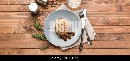 Teller mit leckerem Pilzrisotto auf Holztisch, Draufsicht Stockfoto
