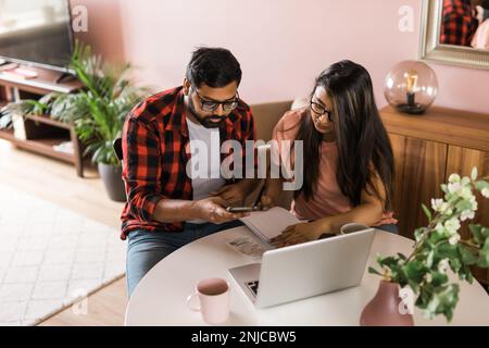 Ernsthafte Ehefrau und Ehemann planen Budget, prüfen Finanzen, fokussierte junge Frau mit Online-Rechner und Zählen von Rechnungen oder Steuern, Mann mit Laptop Stockfoto