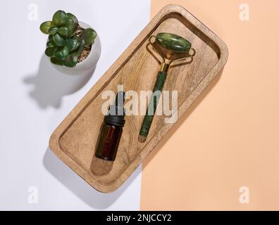 Handmassagegerät für das Gesicht und braune Glasflasche mit Tropfen auf Marmorplatte, Draufsicht Stockfoto