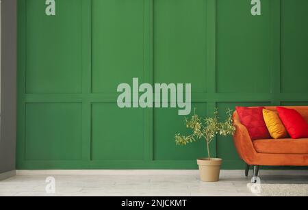 Rotes Sofa mit stilvollen Kissen und Zimmerpflanzen an grüner Wand Stockfoto