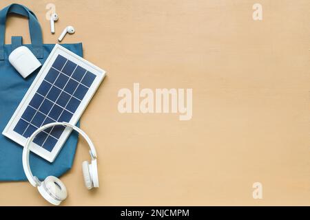Komposition mit tragbarem Solarpanel, kabellosen Kopfhörern und Tasche auf beigefarbenem Holzhintergrund Stockfoto