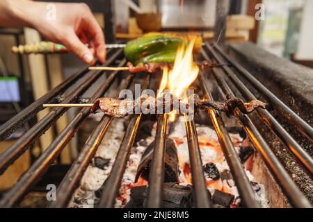 Ein Koch, der Fleischspieße dreht, die auf Holzkohlen kochen Stockfoto