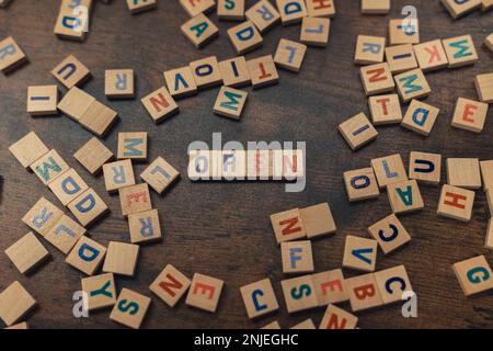 Offenes Wort mit Scrabble-Fliesen auf einem Holztisch und anderen verstreuten Fliesen. Hochwertiges Foto Stockfoto