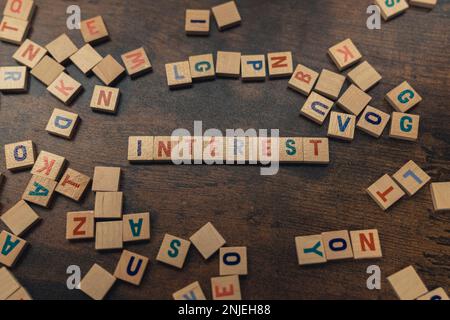 Zinsen geschrieben mit Scrabble-Fliesen auf einem braunen Holztisch, verstreut mit Alphabeten. Hochwertiges Foto Stockfoto