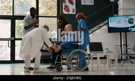 Junger Mann und Frau, die alten Erwachsenen helfen, an der Check-up-Konsultation teilzunehmen, bringen kranken Patienten mit Herzproblemen in die medizinische Einrichtung. Arzt, der eine Person mit Sodbrennen untersucht. Stockfoto