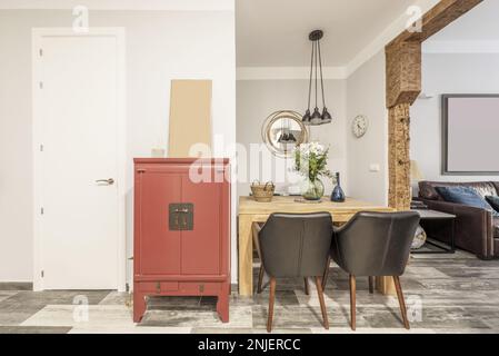 Esstisch aus massivem Holz neben einem roten Sideboard im asiatischen Stil in einem Raum mit massiven Holzsäulen Stockfoto