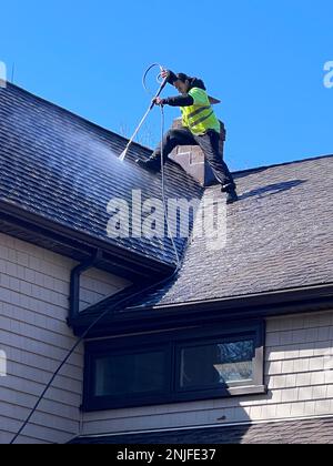 Ein Latino-Arbeiter, der das Dach eines Wohnhauses mit Strom wäscht, um Schimmel und Moos zu entfernen. Stockfoto