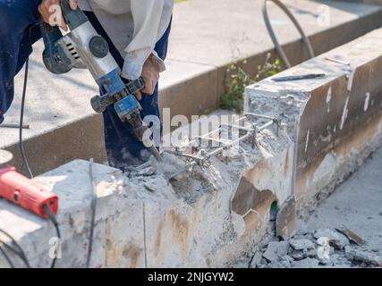 Arbeiter, der einen elektrischen Bohrhammer zum Schneiden des Betonsteins für die Wand verwendet, Nahaufnahme Stockfoto