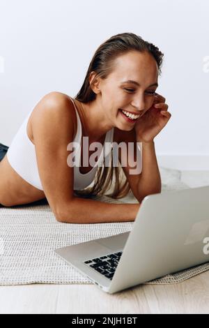 Frau, die zu Hause mit einem Freiberufler arbeitet, der zu Hause mit einem Laptop arbeitet und online auf dem Boden liegt und mit Zähnen lächelt Stockfoto