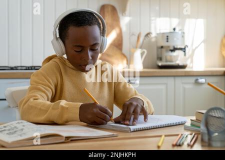 Fokussierter afrikanischer Junge, der am Schreibtisch sitzt und an einem technischen Projekt arbeitet, technische Zeichnungen für Kinder Stockfoto