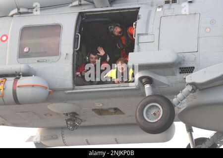 USA Küstenwache Petty Officer 3. Klasse Matthew Abban, derzeit auf USCGC Bear (WMEC 901) für seine Patrouille eingesetzt, winkt seinen Kameraden aus einem MH-60R Hubschrauber der Royal Danish Navy während einer Fotoübung in Operation Nanook, Nordatlantik, 6. August 2022. Abban ist Spezialist für öffentliche Angelegenheiten der Küstenwache. Stockfoto