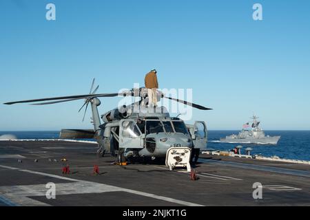 230207-N-PQ495-1273 PAZIFIK (7. Februar 2023) Seeleute an Bord des Flugzeugträgers USS Carl Vinson der Nimitz-Klasse (CVN 70) führen Wartungsarbeiten an einem MH-60s Sea Hawk durch, der an den "Schwarzen Rittern" des Helicopter Sea Combat Squadron (HSC) 4 befestigt ist, während Arleigh Burke-Klasse Guided-Missile Destroyer USS Sterett (DDG 104) neben DDG fährt. Vinson führt derzeit routinemäßige Seeeinsätze durch. (USA Marinefoto von Mass Communication Specialist 3. Class Larissa T. Dougherty) Stockfoto