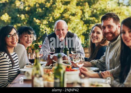 Ich bin ein glücklicher Mann, wenn ich meine Familie um mich habe. Eine Gruppe von Personen, die während eines Festmahls an einem Esstisch zusammen sitzen. Stockfoto