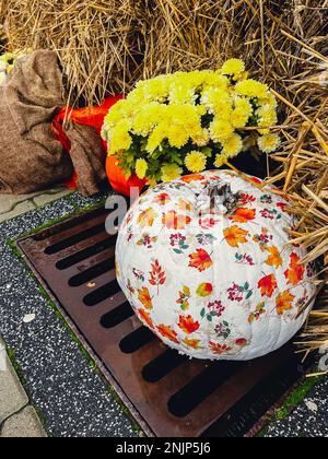 Wunderschön bemalte Kürbisse in Blumen rustikale Heudekoration im Freien. Stilvolles Herbstdekor des Außengebäudes. Ländliche Einrichtung auf Heuhaufen in der Straße. Herbsternte Thanksgiving und Halloween Feiertagsvorbereitungen. Stockfoto