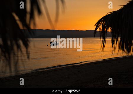 Sonnenaufgang auf dem Meer auf einer Kette von Hügeln, der ganze Himmel scheint in einer intensiven goldenen Orange und spiegelt sich im Wasser, auf dem Meer ein kleines Boot in der for Stockfoto