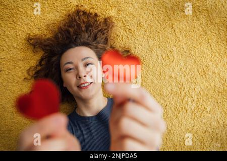 Asiatische Frau mittleren Alters, die zwei rote Herzen in der Hand hält. Das Konzept der guten Taten mit Liebe, Blutspende und Nächstenliebe. Unschärfe-Effekt, Draufsicht Stockfoto