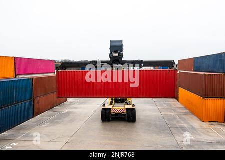 Transporthintergrund einer schweren Hubmaschine, die Transportbehälter um ein kommerzielles Dock transportiert, um auf der Schiene oder Straße weiterzutransportiert werden zu können Stockfoto