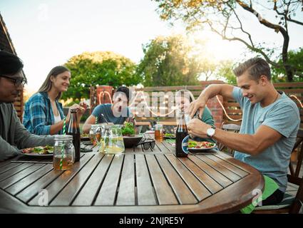 Freunde und Essen. Eine junge Gruppe von Freunden, die zusammen eine Mahlzeit genießen, während sie draußen an einem Tisch in einem Garten sitzen. Stockfoto