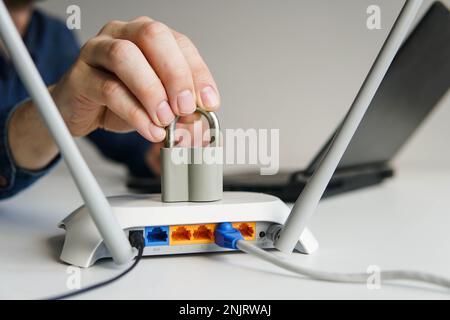 Hochgeschwindigkeits-wlan-Router mit Schloss. Mann, der im Hintergrund ein Notebook benutzt. Passwortgeschütztes WLAN-Netzwerk und Internet-Zensur-Konzept. Stockfoto