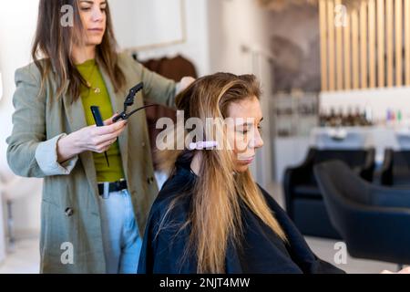 Friseur in Freizeitkleidung, der die Haare einer Kundin in Strähnen teilt, bevor er sie in einem modernen Kosmetikstudio färbt Stockfoto