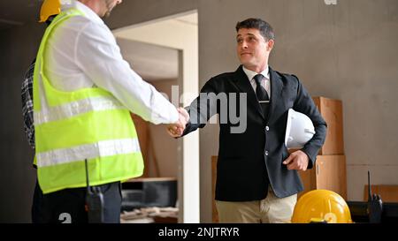 Selbstbewusster weißer Geschäftsmann im formellen Business-Anzug, der während des Treffens auf der Baustelle einem Bauingenieurleiter die Hand schüttelt. Stockfoto