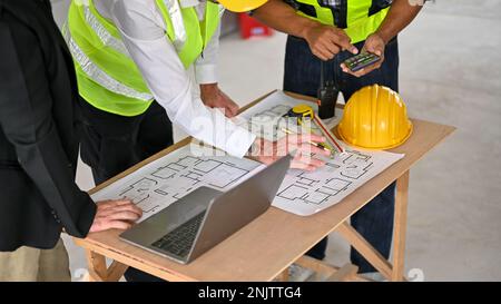 Ein abgeschnittenes Bild einer Gruppe professioneller Bauingenieure und eines Geschäftsmanns, der sich auf einer Baustelle trifft, um die Größe des Gebäudes auf einer Blase zu überprüfen Stockfoto