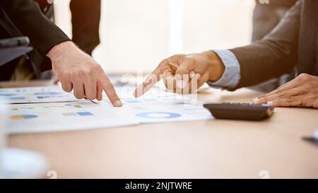 Geschäftsleute zeigen mit dem Finger auf einen Finanzbericht, diskutieren und teilen Ideen, während sie die Finanzstrategie im Meeting analysieren und planen. cr Stockfoto