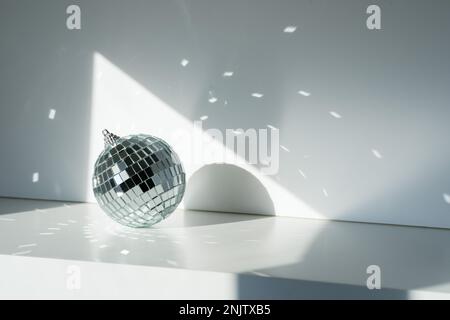 Diskokugel im Sonnenlicht mit Reflexionen auf weißem Hintergrund. Geometrische Schatten Stockfoto