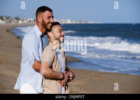 Ein reizendes schwules Paar, das am Strand zusammen gelächelt hat. Stockfoto