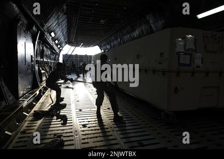 Ein Flugzeugführer der 380. Expeditionary Logistics Readiness Squadron und der 60. Aircraft Maintenance Squadron arbeiten zusammen, um eine General Atomics MQ-9 Reaper Drohne an Bord einer Lockheed C-5M Super Galaxy zu bringen, die der 22. Airlift Squadron am 10. August 2022 auf dem Luftwaffenstützpunkt Al Dhafra, Vereinigte Arabische Emirate, zugewiesen wurde. Die Reaper können zur schnellen Wiederverwendung in Lagerbehälter, sogenannte „Särge“, zerlegt werden. Stockfoto