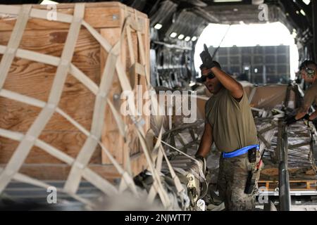 Staff Sgt. Rayan Rahman, ein Vorfeldleiter, leitet einen K-Loader-Betreiber während der Entgegennahme der Fracht von einer Lockheed C-5M Super Galaxy, die der 22. Luftwaffenstaffel am 10. August 2022 am Luftwaffenstützpunkt Al Dhafra, Vereinigte Arabische Emirate, zugewiesen wurde. Die für den Vorfeldbetrieb zuständigen Aufsichtspersonen sind mit der sicheren Handhabung der Fracht und der Sicherheit des Personals des Air Terminal Operations Center betraut. Stockfoto