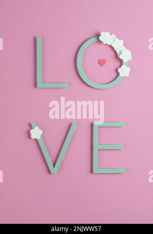 Romantische Komposition in Pastelltönen mit Schriftzug „Love“, Illustration aus Papier auf pinkfarbenem Hintergrund. Stockfoto